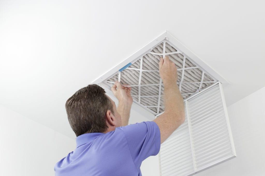 A person in a blue shirt replaces an air filter in a ceiling vent to ensure the heating system runs efficiently during the cold Maryland winters.