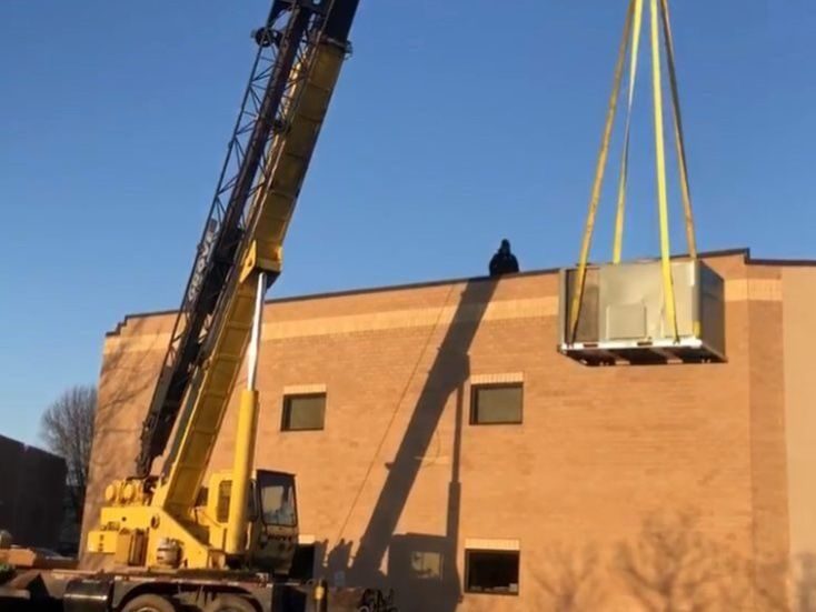 Crane lifting commercial HVAC unit to place on roof.