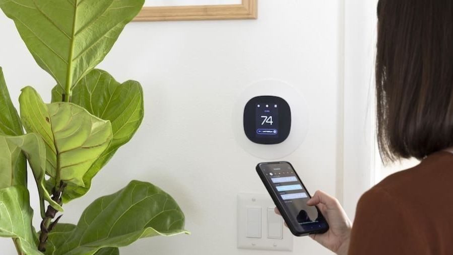 Homeowner holding phone to adjustt smart thermostat.